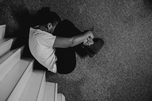 Hombre sentado en el suelo en posición fetal, mostrando tristeza y vulnerabilidad emocional.