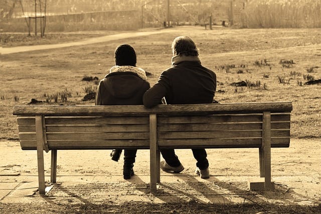 Dos personas sentadas en un banco conversando de manera cercana y sincera, compartiendo emociones y pensamientos en un entorno tranquilo.
