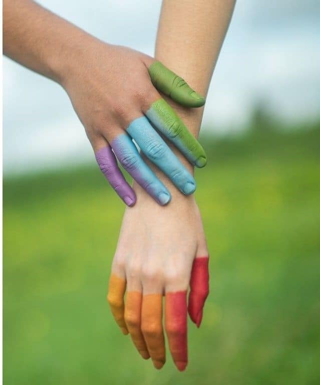 Manos de una niña y un adulto entrelazadas, la niña sujeta la muñeca del adulto con delicadeza, dedos pintados de colores, simbolizando protección, vínculo y conexión emocional.
